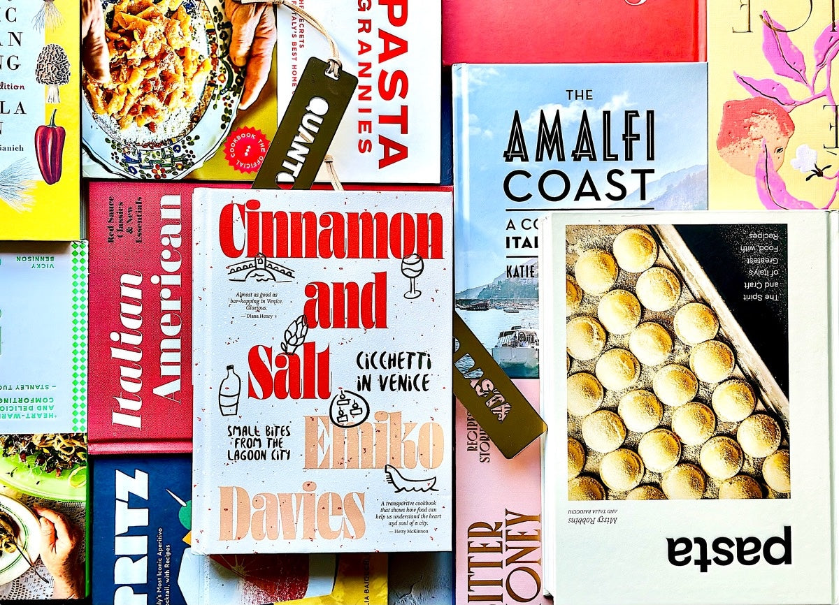 We a see an assortment of Italian cookbooks, stacked next to and on top of each other. 